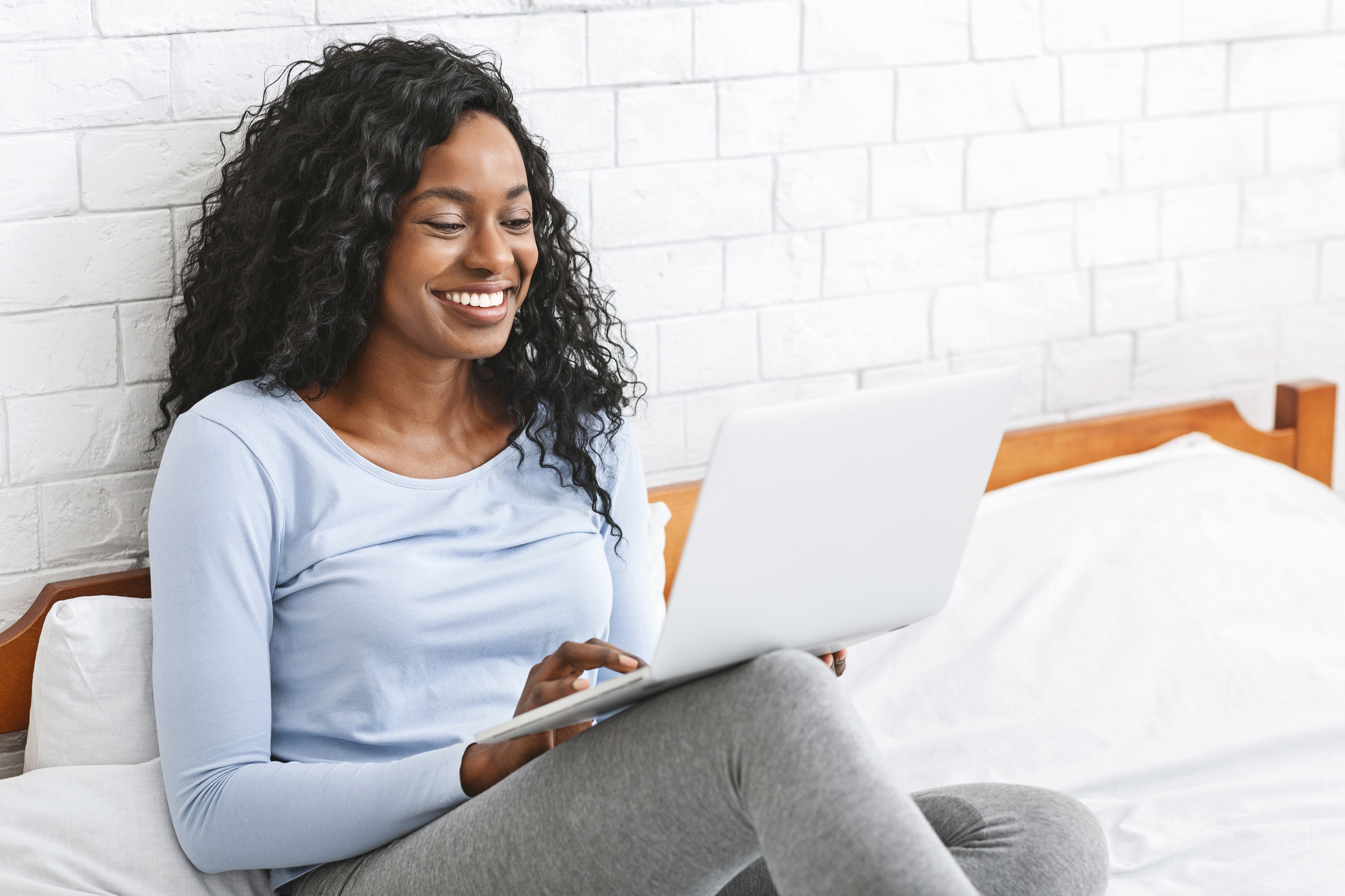 Smiling young lady chatting online in bedroom